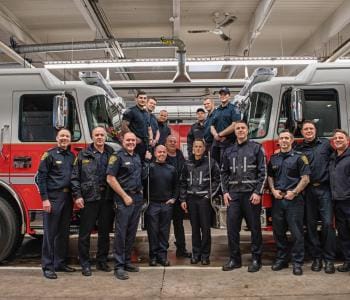 Firefighters posing in front of two firetrucks