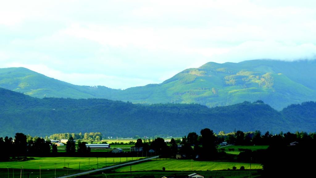 Scenic view of Sumas Mountain in Abbotsford, with rolling green hills, farmland, and a rural road stretching through the valley.
