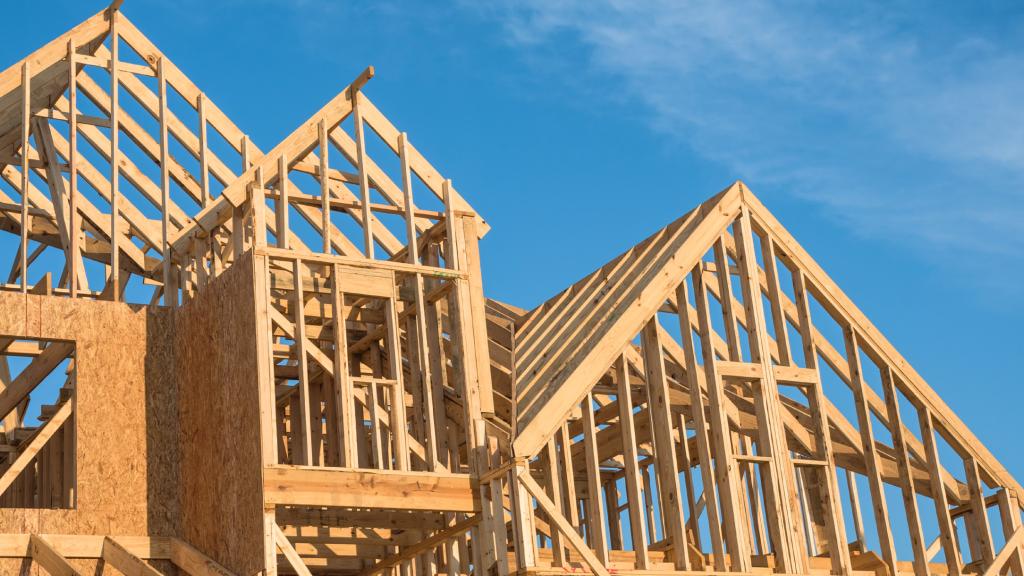 Wooden house frame under construction with clear blue sky background – residential building project in progress.