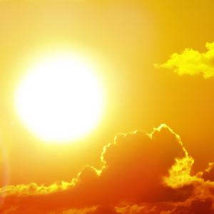 A close-up of the sun shining brightly in a clear sky with a few clouds.