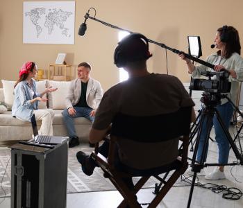 film crew inside someone's home filming people talking on the couch
